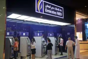 People using ATMs at an Emirates NBD branch, with a blue and white sign overhead.