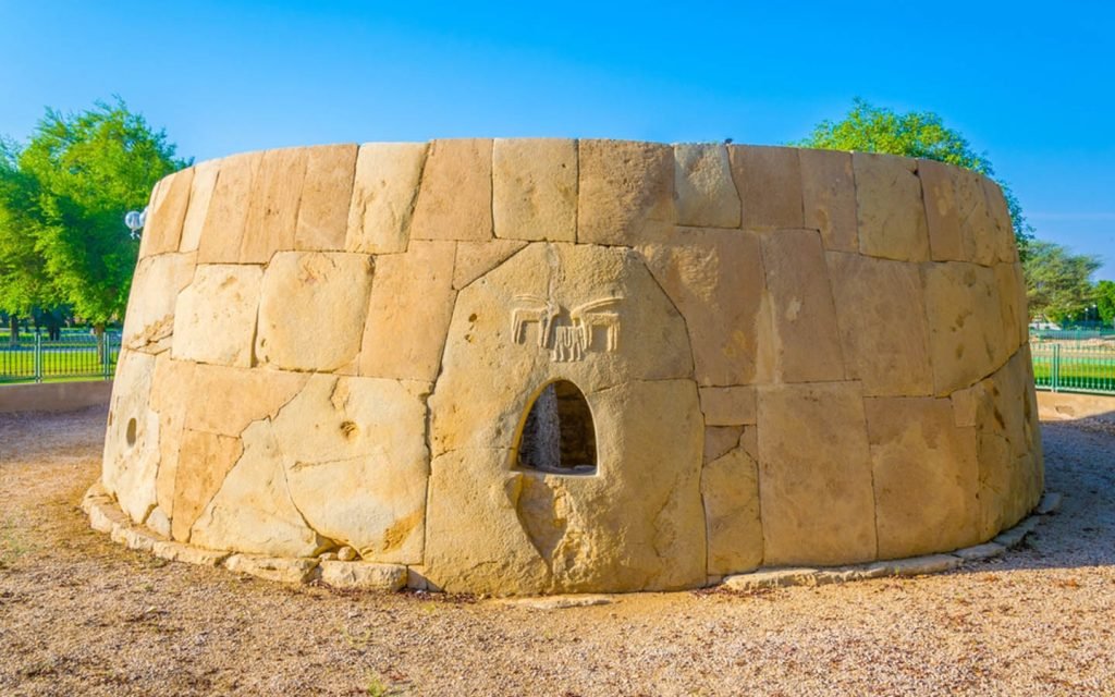 A round stone structure with a small arched opening in a park under a blue sky