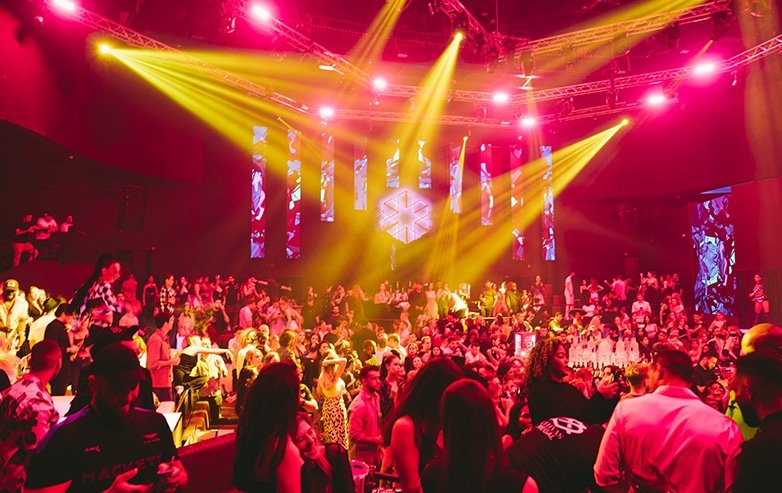 Crowded nightclub or concert venue with bright pink and yellow stage lights over the audience