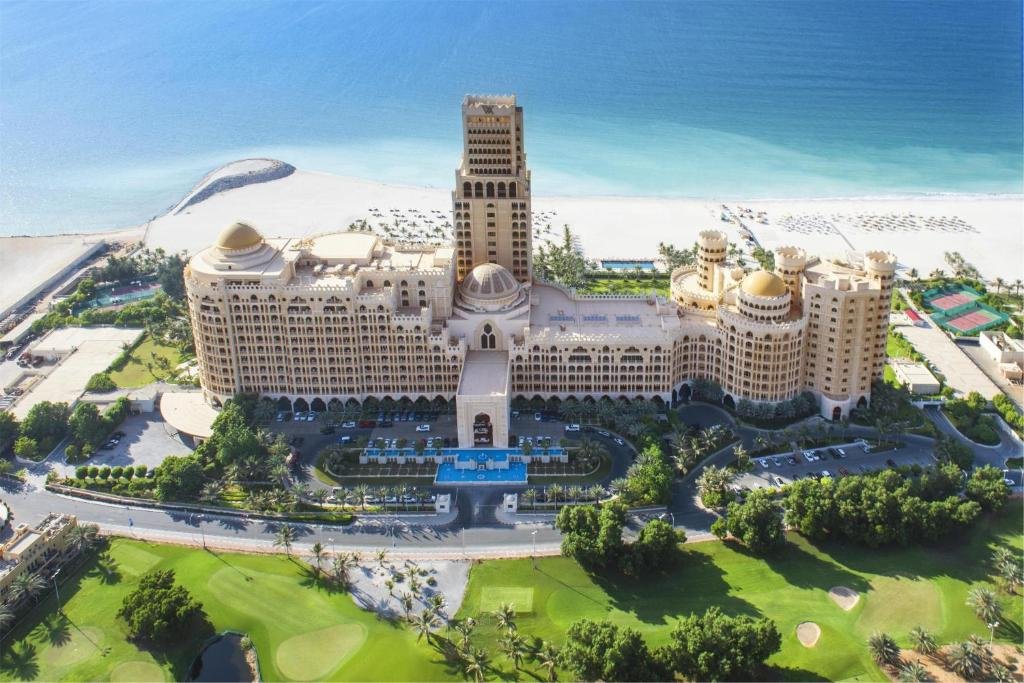 Aerial view of a large beachfront resort with domed towers, gardens, golf greens, and turquoise sea beyond