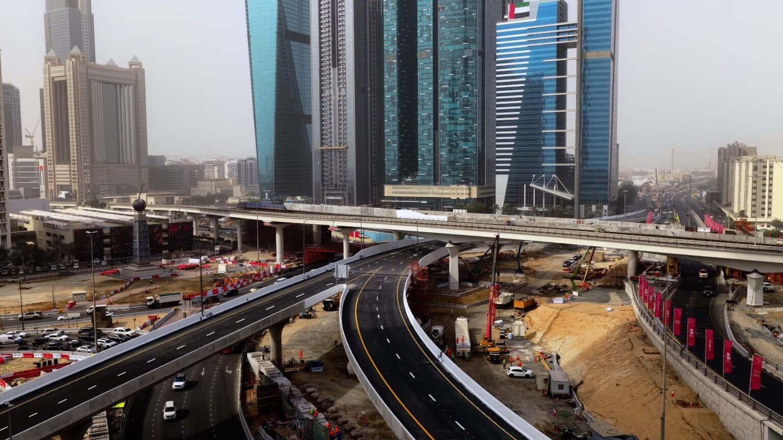 Aerial view of a busy urban construction site with overpasses, surrounded by tall modern skyscrapers.