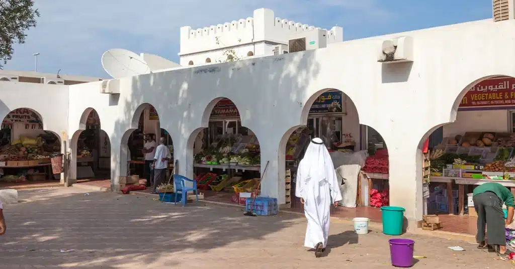 Open-air market with arched stalls selling fruits and vegetables, and people walking in the foreground