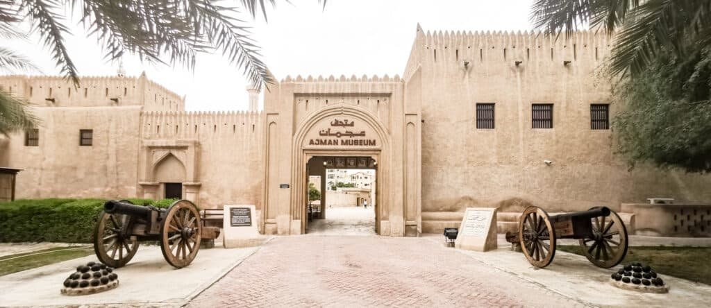 Entrance to Ajman Museum with historic fortress walls and two old cannons flanking the gate