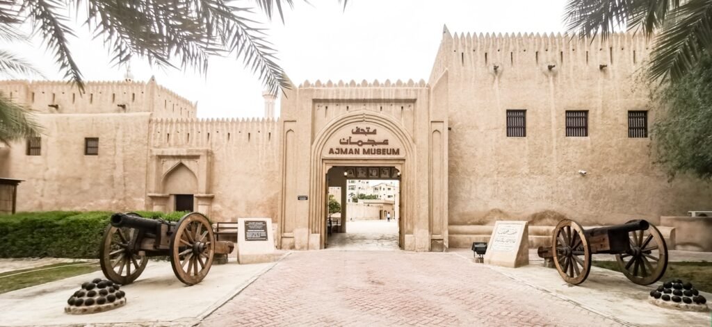 Entrance to Ajman Museum with historic beige fort walls and cannons on either side