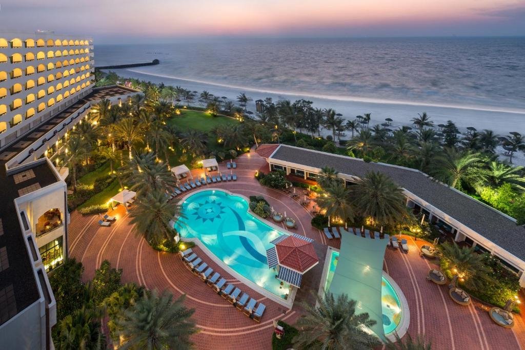 Sunset view of a seaside resort with a lit pool, palm trees, and the ocean beyond