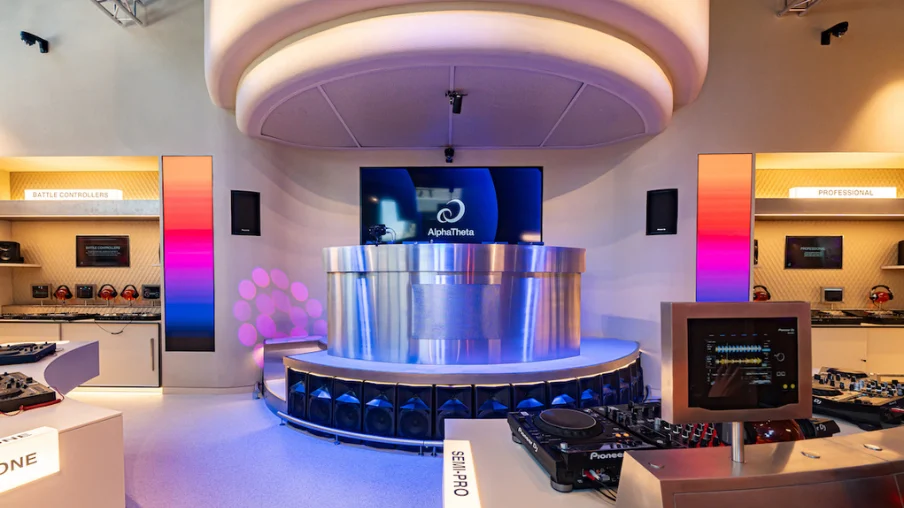 Futuristic AlphaTheta DJ booth with Pioneer equipment, colorful LED panels, and an AlphaTheta screen in a showroom