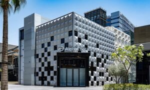 Modern geometric building with a faceted silver facade and glass entrance in an urban plaza