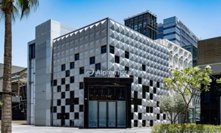 Modern geometric building with a faceted silver facade and glass entrance in an urban plaza