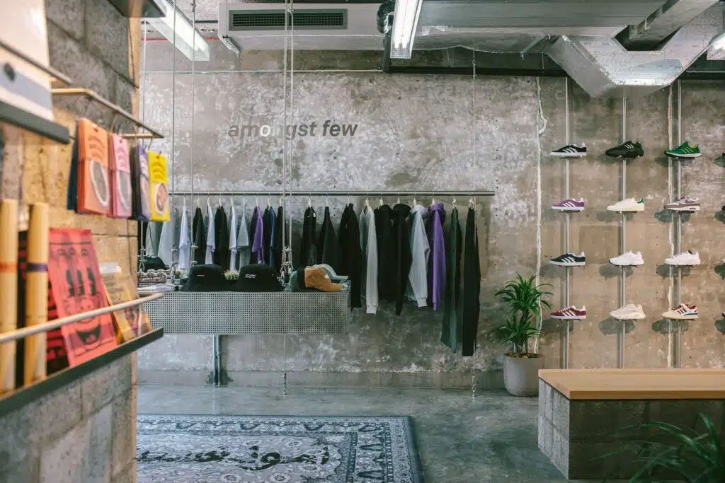 Minimalist sneaker and streetwear store interior with concrete walls, hanging clothes, and shoes on display