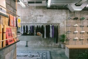 Minimalist sneaker and streetwear store interior with concrete walls, hanging clothes, and shoes on display