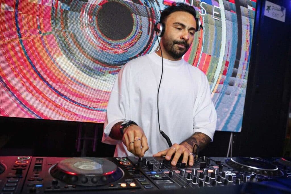 DJ wearing headphones mixing music on a controller in front of a colorful abstract screen