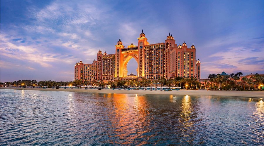 Best Brunch in Dubai: Illuminated Atlantis beachfront resort with a large arch-shaped tower reflected in calm water at dusk