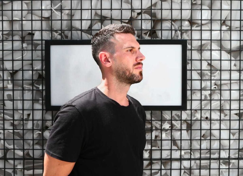 Bachir Salloum in a black T-shirt in profile against a wall of white light bulbs in wire grids