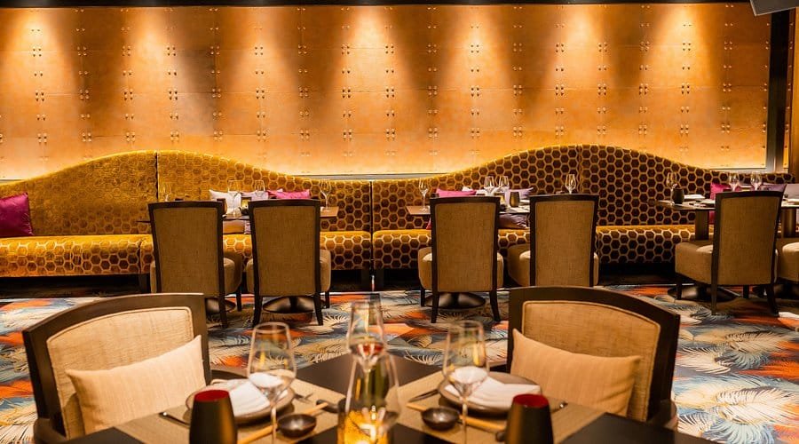 Upscale restaurant dining area with patterned sofas, empty chairs, and set tables under warm lighting