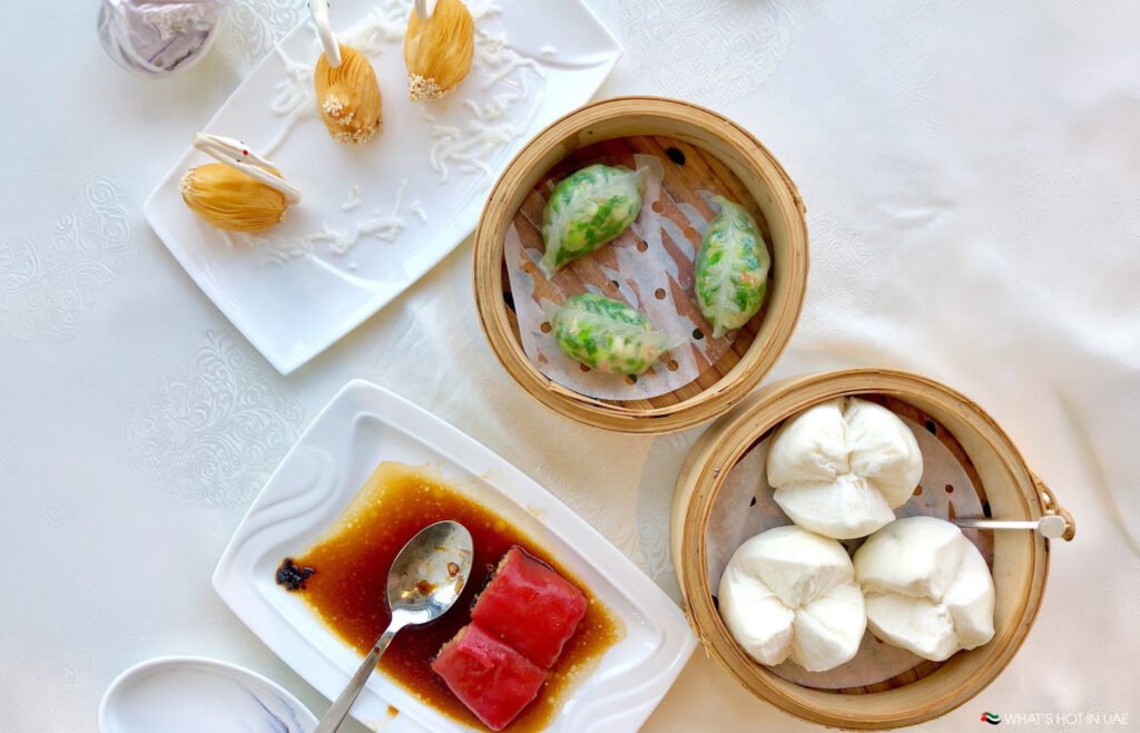 Assorted best Chinese restaurants Dubai dim sum on white plates and bamboo steamers, including dumplings and buns with sauce