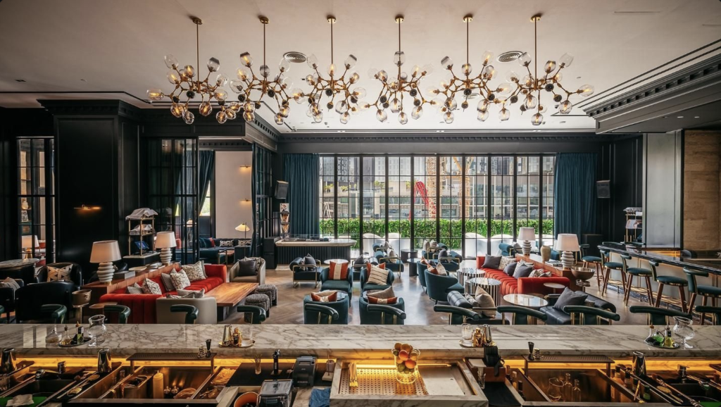 Elegant hotel lounge with colorful seating, a marble bar, and modern chandeliers by large windows