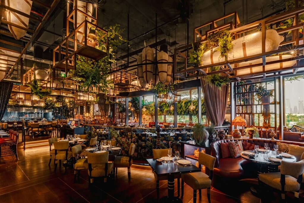 Upscale restaurant interior with warm lighting, hanging plants, and set tables near large windows