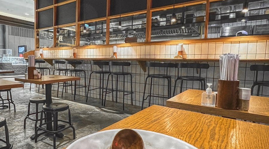 Empty modern cafe with wooden tables, bar stools, and a tiled counter area