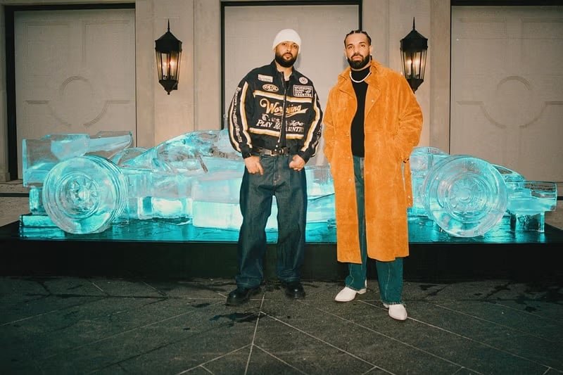 Two men pose in front of a glowing ice sculpture of a sports car