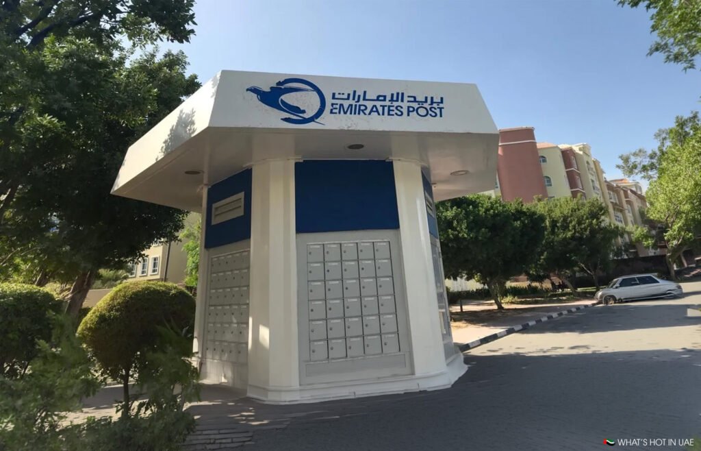 Emirates Post parcel locker kiosk on a sunny street, with trees and apartment buildings nearby
