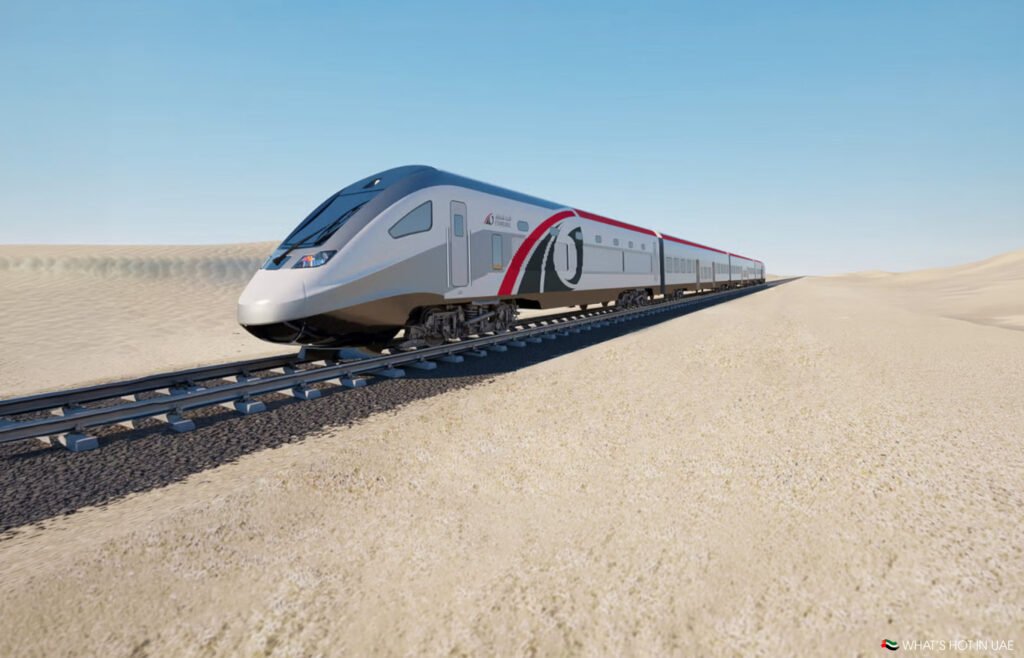 Modern high-speed train traveling through a sandy desert on tracks under a clear blue sky