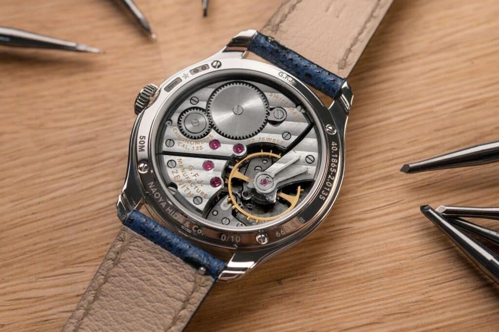 Close-up of a G.F.J. Calibre 135 wristwatch showing its exposed mechanical movement on a wooden surface