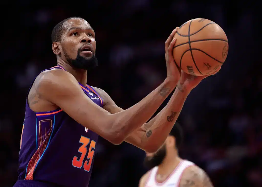 Kevin Durant in a purple jersey preparing a shot while holding the ball near his face