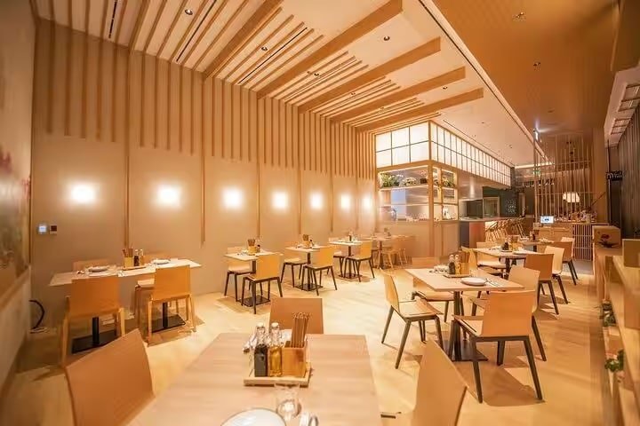 Warmly lit modern restaurant dining room with wooden tables and chairs, set for service in an empty space