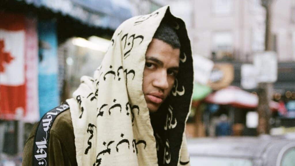 Young man in a patterned hooded scarf looks at the camera on a blurred city street