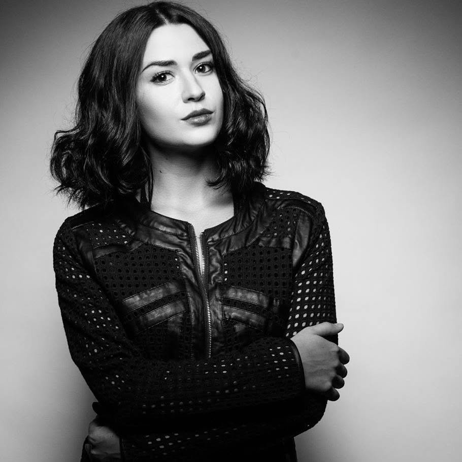 Black-and-white portrait of Masha Vincente with wavy shoulder-length hair wearing a textured leather jacket, arms crossed
