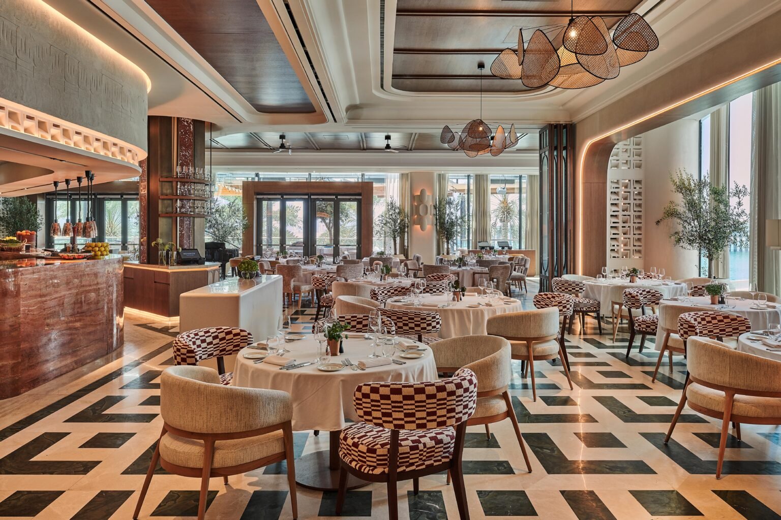 Elegant modern restaurant with set round tables, patterned chairs, and a marble bar under sculptural pendant lights