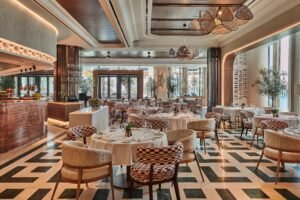 Elegant modern restaurant with set round tables, patterned chairs, and a marble bar under sculptural pendant lights