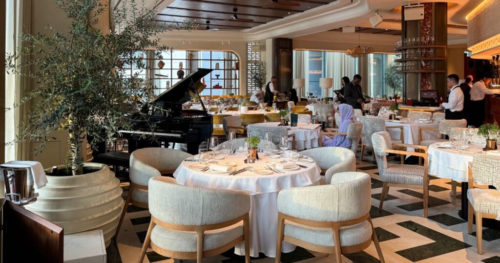 Elegant Novikov Abu Dhabi restaurant dining room with set tables, cushioned chairs, a grand piano, and guests seated near a bar