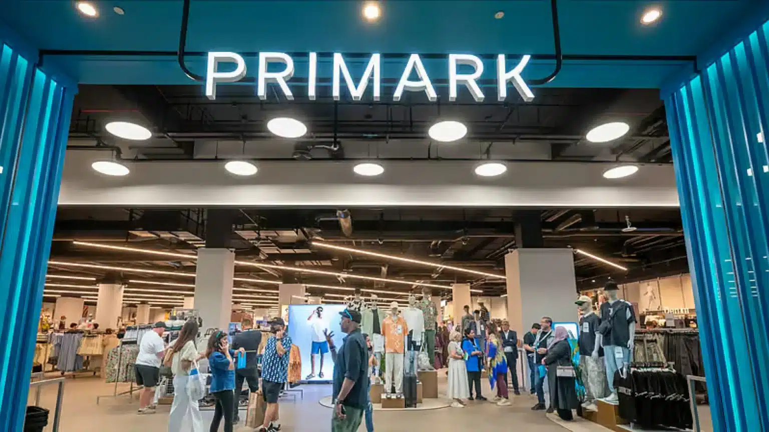 Busy Primark store entrance with shoppers, mannequins, and bright blue framing lights