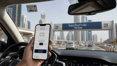 Hand holding a phone showing a toll account top-up screen inside a car approaching a toll gate