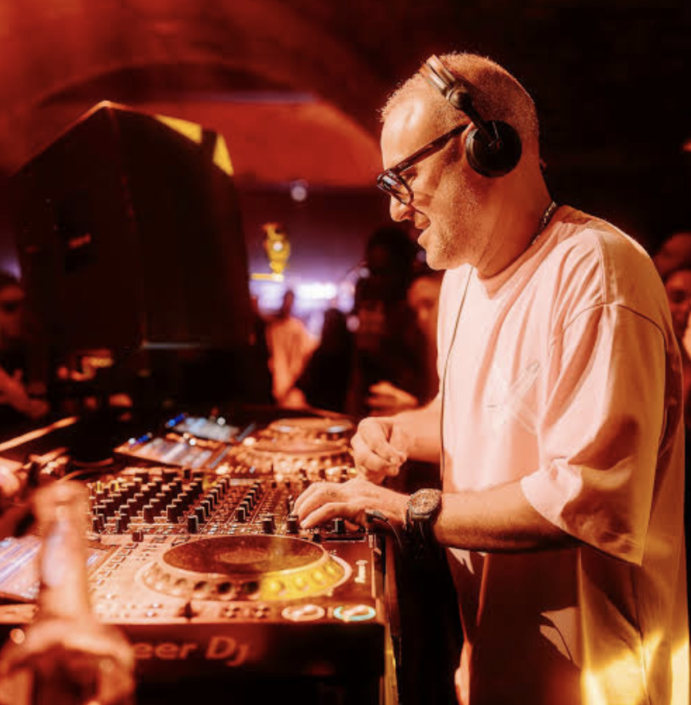 DJ wearing headphones mixes music at a club console under red lighting