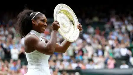 Tennis player Serena Williams smiling and holding up the Wimbledon championship trophy after a win