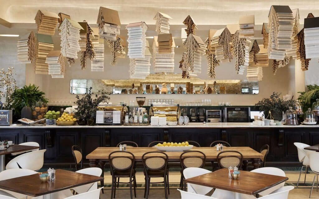 Stylish café with hanging book-like lamps, a long coffee bar, and wooden tables with white chairs