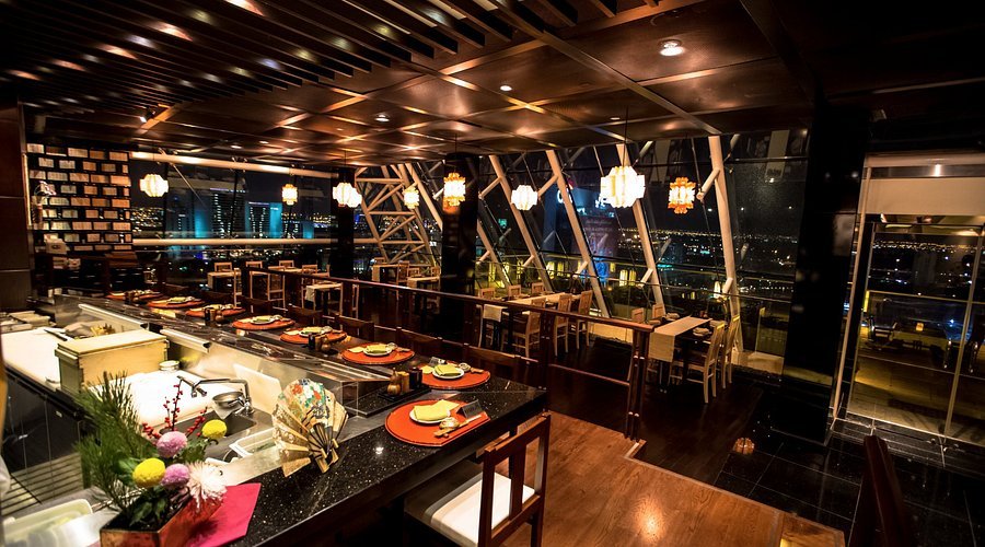 Modern sushi restaurant interior with a sushi counter, warm lighting, and city views through large windows