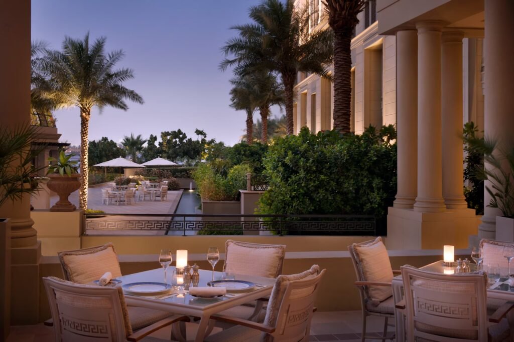 Elegant Vanitas Palazzo Versace Dubai outdoor restaurant patio at dusk with set tables, candles, palm trees, and a resort-style courtyard