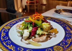 Gourmet seafood salad topped with colorful bell pepper ribbons on a blue-and-gold ornate plate