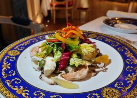 Gourmet seafood salad topped with colorful bell pepper ribbons on a blue-and-gold ornate plate