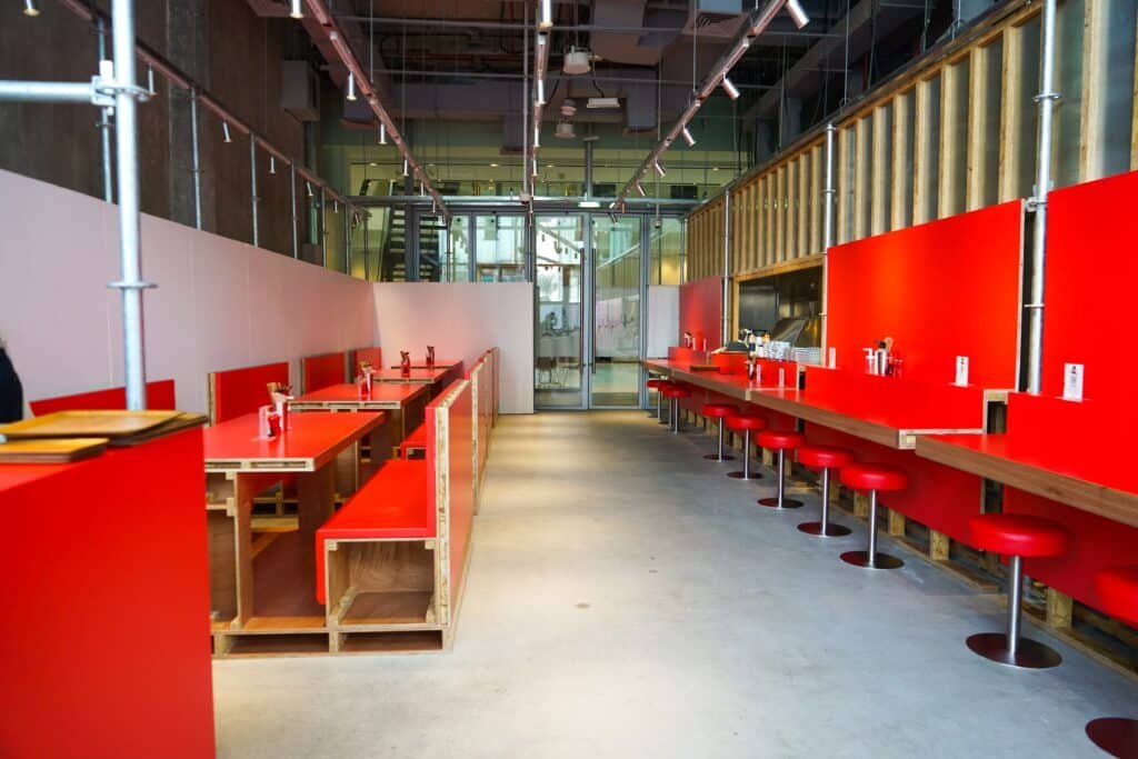 Modern restaurant interior with bright red booths, a long counter with stools, and glass doors at the back