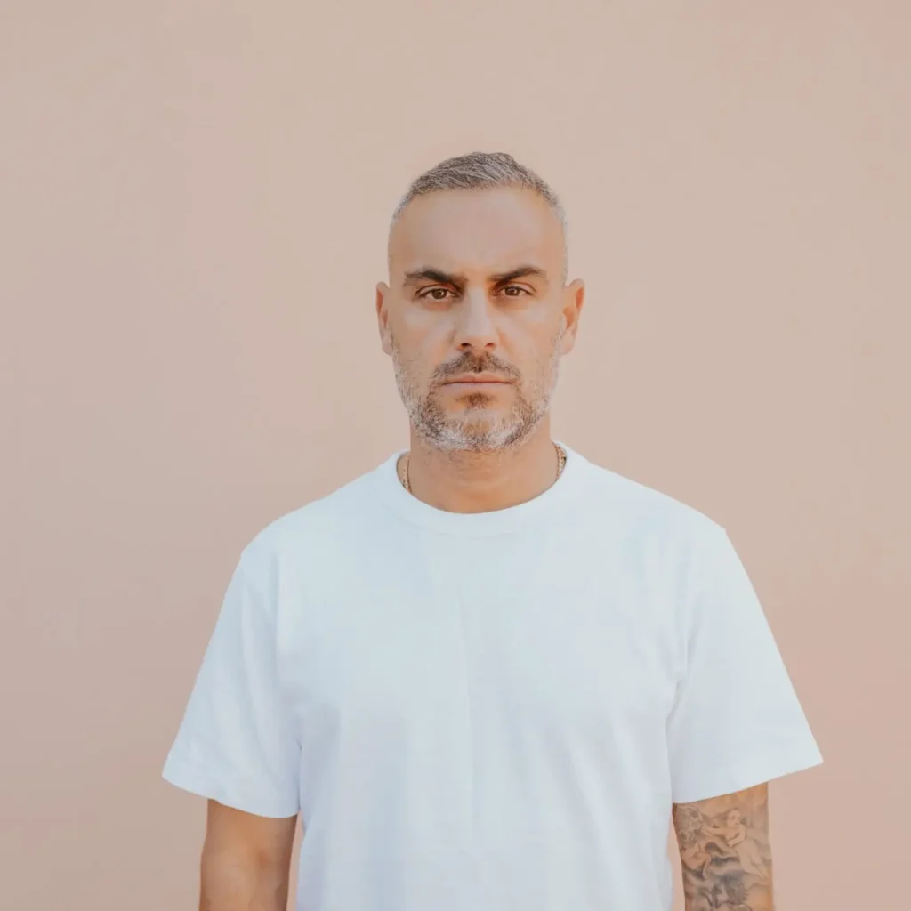 Portrait of BADBOX in a white T-shirt standing against a plain beige background