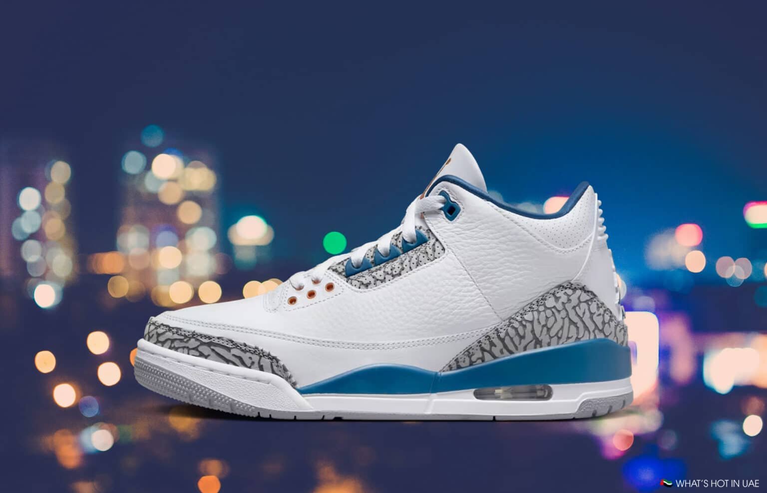 White and blue sneaker with elephant-print accents against a blurred city lights background