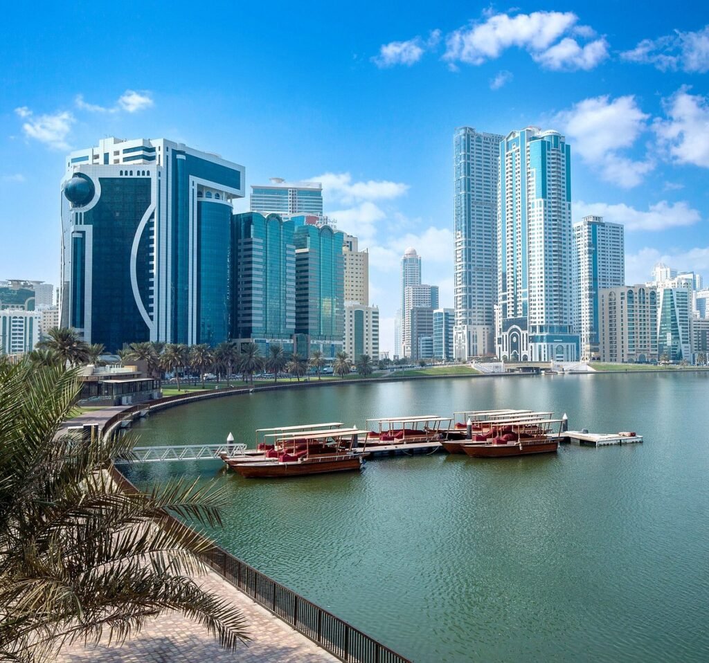 Al Majaz skyline with high-rise buildings, a calm bay, and docked boats under a blue sky
