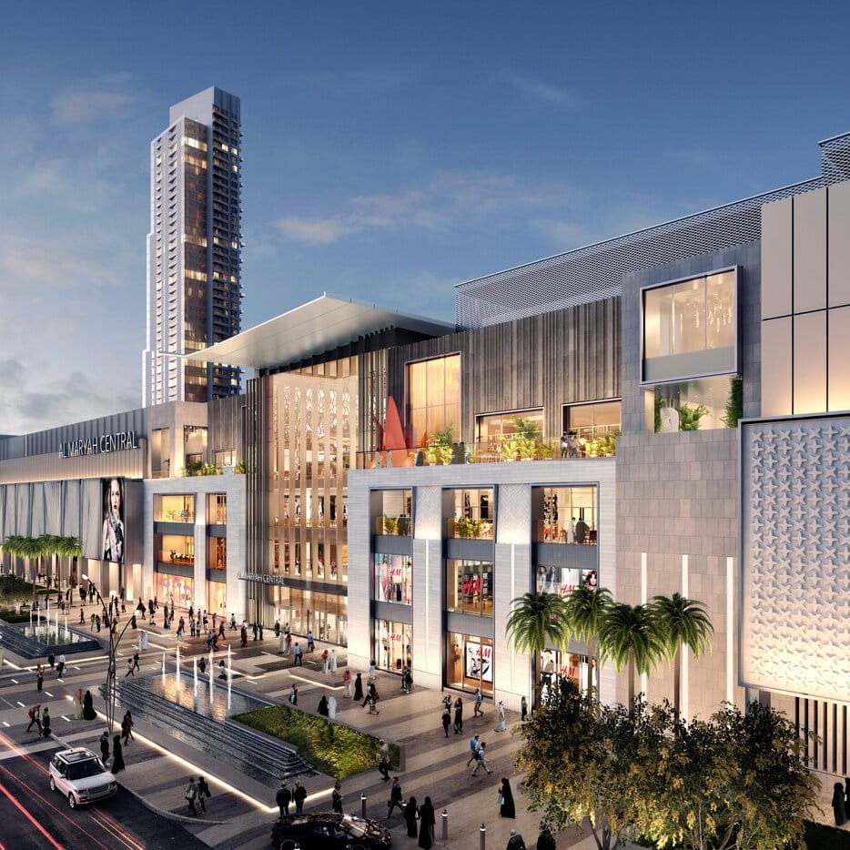 A modern Al Maryah Island shopping mall with bright storefronts, palm trees, and a tall tower rising behind it at dusk
