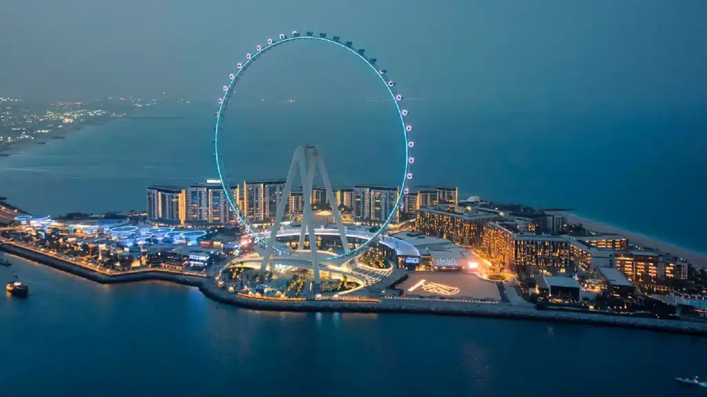 A giant illuminated Ferris wheel rises over Bluewaters Island at dusk