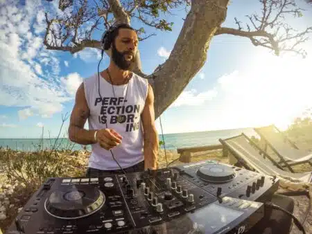DJ in headphones mixing music outdoors by the beach at sunset