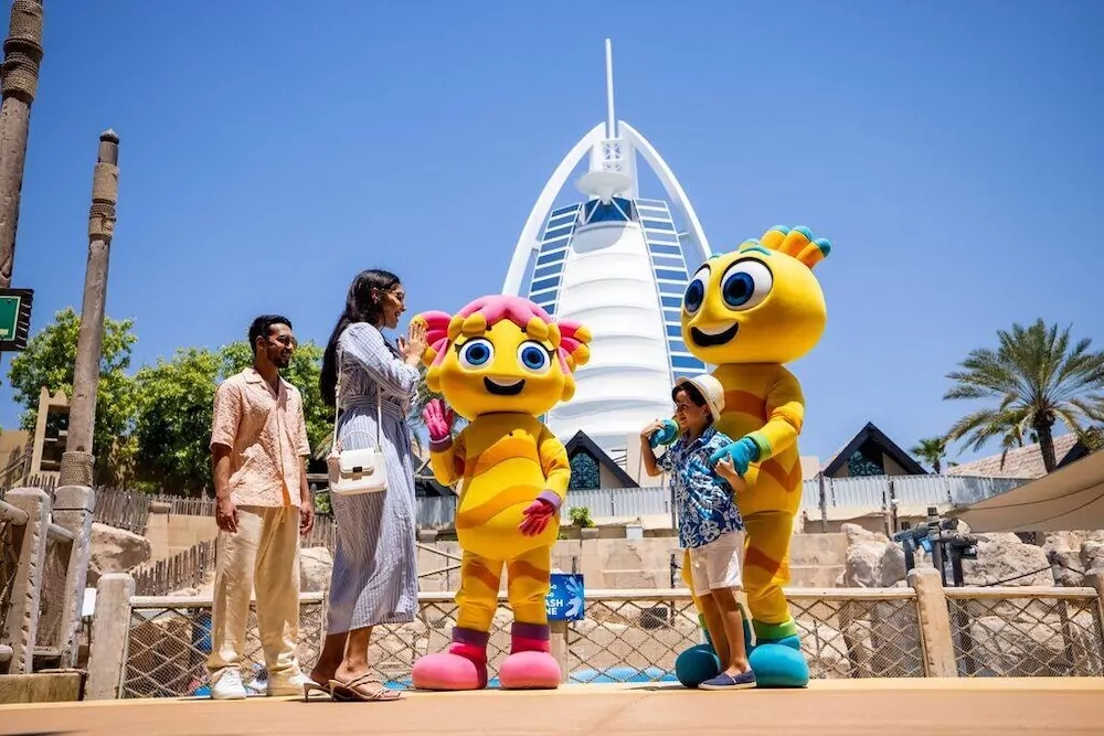 Family posing with colorful mascot characters in front of the Burj Al Arab hotel